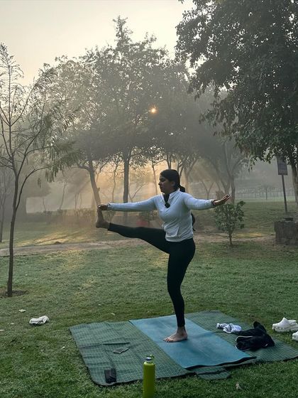 Holding a standing leg raise against a backdrop of sunlit trees.