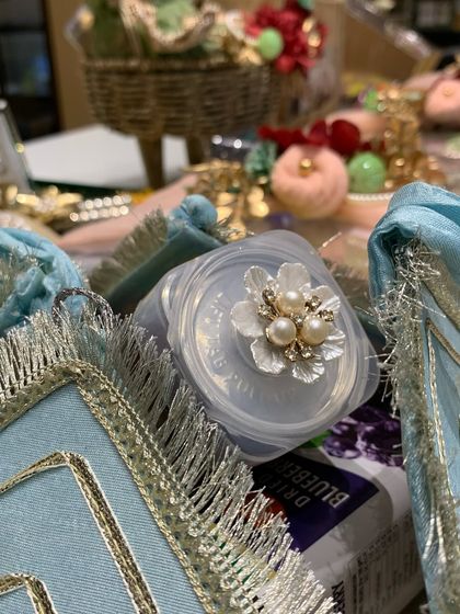 A close-up of a small, decorated container, part of a larger trousseau. The pearl and crystal flower on top shows our commitment to making every detail beautiful.