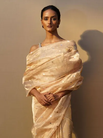 A shimmering gold tissue saree styled with a dramatic drape over the shoulder, accented by a simple brooch for a touch of elegance.