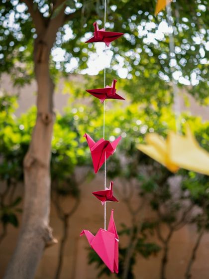 A string of red origami cranes hanging from a tree, a symbol of good luck and happiness.