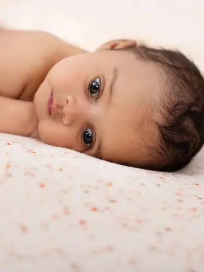 A simple, beautiful portrait of a newborn lying on a speckled blanket. This minimalist shot focuses entirely on the baby's delicate features and soulful eyes.
