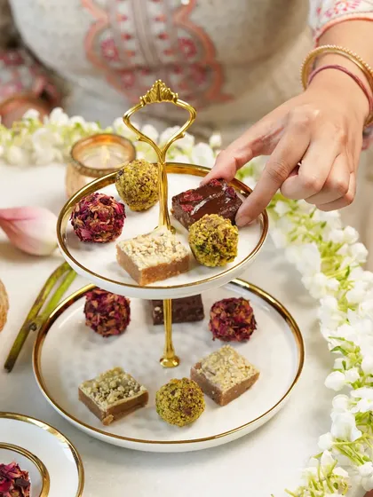 A hand selecting a piece of mithai from a two-tiered platter. This shot is elegant and focuses on the beauty of the festive sweets.