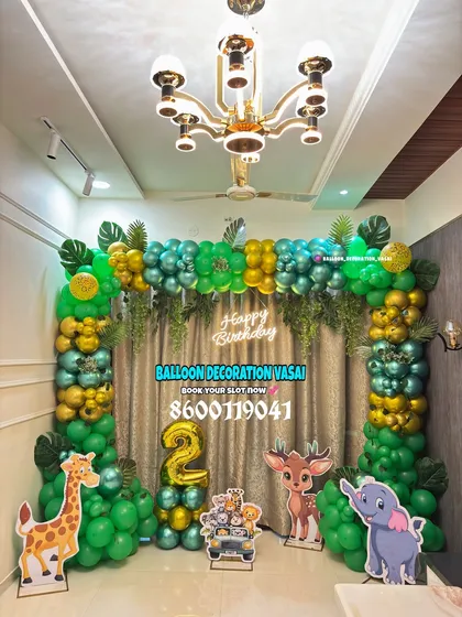We brought the jungle to life for this 2nd birthday party. This setup includes a full balloon arch with green, gold, and teal chrome balloons, jungle leaf accents, and life-sized cutouts of a giraffe, deer, and elephant.