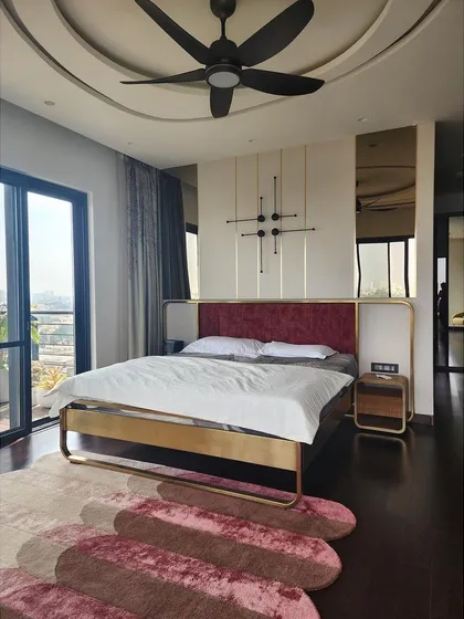 This master bedroom features a custom bed with a striking brass frame and a deep red velvet headboard. The design is complemented by a kinetic wall sculpture and integrated side tables, creating a look that is both luxurious and artistically curated.