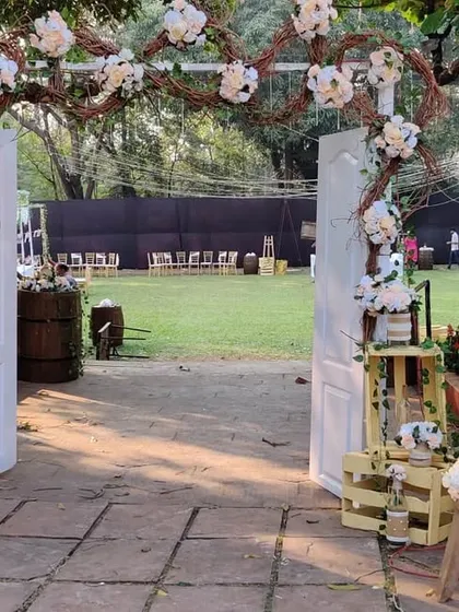 This rustic entrance features a freestanding white door, a welcome sign on an easel, and charming details like wooden crates and a ladder used as shelving for floral arrangements.