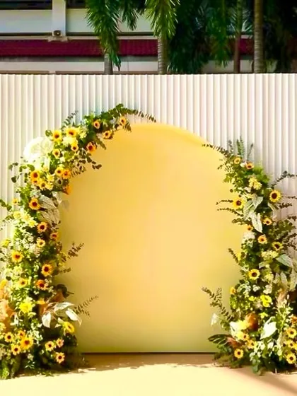 A minimalist and modern Haldi stage. The design features a simple arched backdrop in sunny yellow, beautifully accented with a semi-arch of sunflowers and greenery.