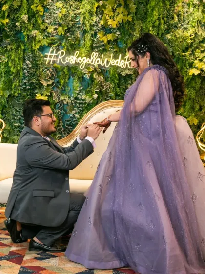 The groom on one knee, proposing to his bride against a lush green wall with a neon sign. A modern and stylish engagement shot.
