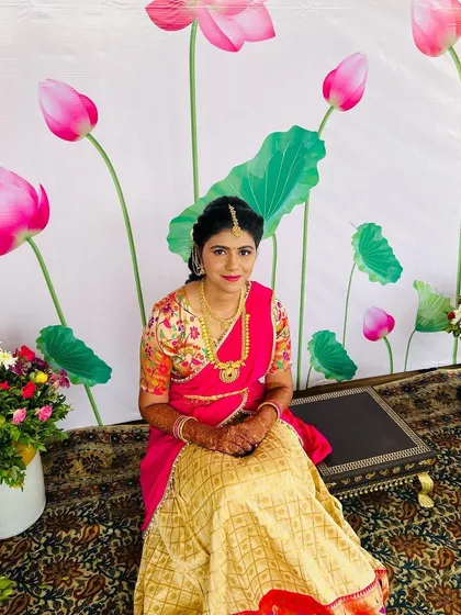 The bride looks so pretty and elegant in her half saree, seated against a lovely floral backdrop.