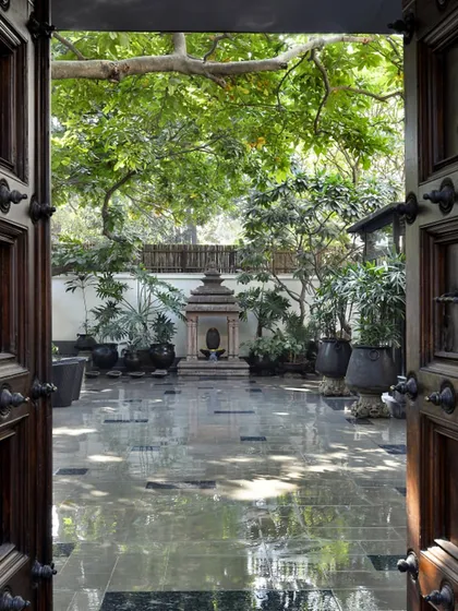 The entrance to the Courtyard Home is a narrative of heritage and tranquility. Framed by old Chettinad doors and teak columns from Kerala, the view opens to a courtyard centered around a temple replica, immediately grounding the home in a rich, cultural context and a sense of peace.