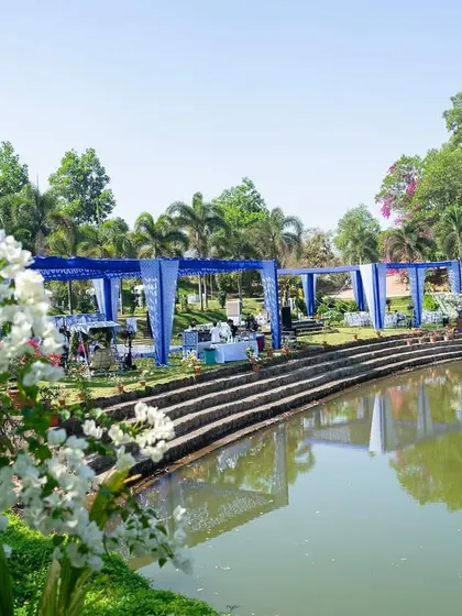 A wide view of the blue and yellow themed Haldi setup by the lake, showing how the bold colors create a stunning contrast with the natural greenery and water.