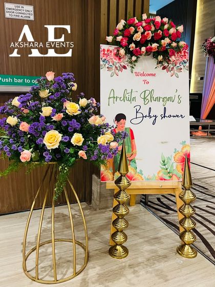 An elegant welcome sign for a baby shower, decorated with fresh flowers. The sign is flanked by traditional brass lamps, creating a beautiful and auspicious entrance.