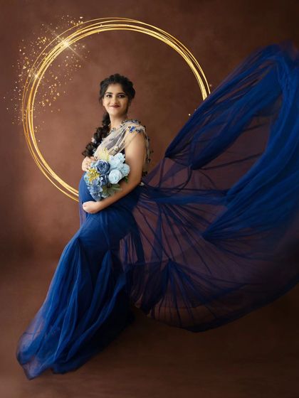 A magical portrait of a mom-to-be in a flowing blue gown, with a sparkling golden halo effect and a bouquet of blue flowers.