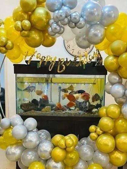 A unique birthday setup framing a fish tank with a gold and silver balloon arch.