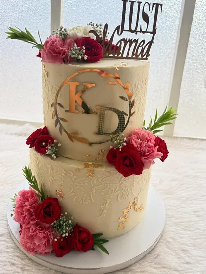 A classic two-tier wedding cake for a beautiful celebration. I used fresh red and pink carnations, a custom monogram, and delicate gold leaf accents to create a design that is both elegant and personal.