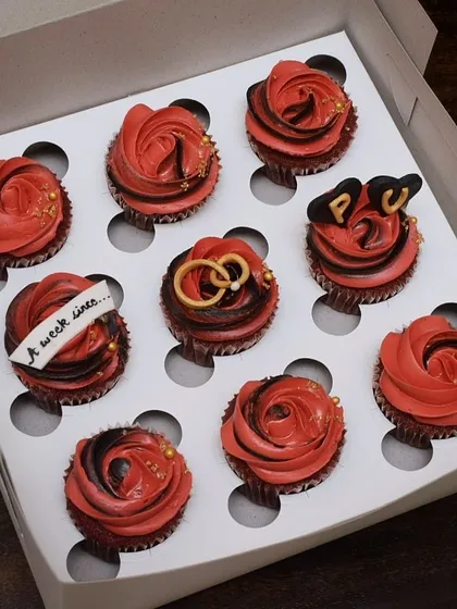 Celebrating new beginnings with this custom engagement cupcake box. The set features rich red velvet cupcakes with red and black frosting, accented with edible gold dust, and detailed fondant work like intertwined rings and custom initials.