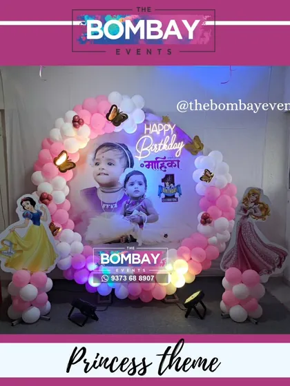A still shot of this beautiful princess-themed first birthday. The setup includes a custom photo backdrop, a pink and white balloon ring, and cutouts of Snow White and Sleeping Beauty.