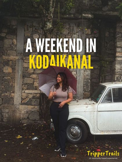 A weekend in Kodaikanal. A woman with an umbrella stands next to a vintage car, capturing the charming, old-world vibe of this hill station.
