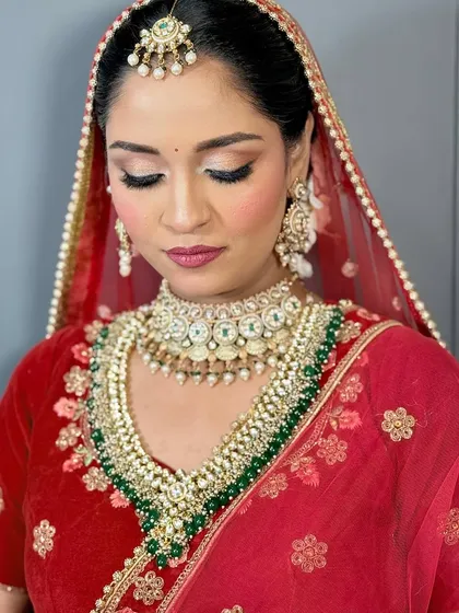A classic North Indian bridal look with a red velvet lehenga. The eye makeup is soft and defined, paired with a rosy lip, perfect for a traditional ceremony.