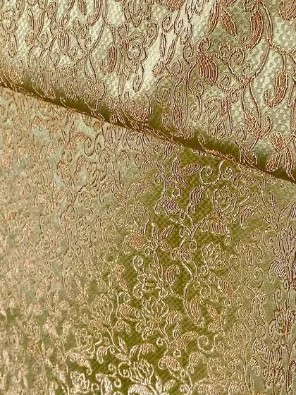 A detailed view of a gold and green brocade fabric, showcasing the intricate texture and sheen that makes it perfect for high-end festive garments.
