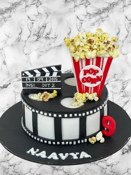 Lights, camera, action! A movie-themed cake for Naavya's 9th birthday, complete with a film reel, a clapperboard, and a big box of popcorn.