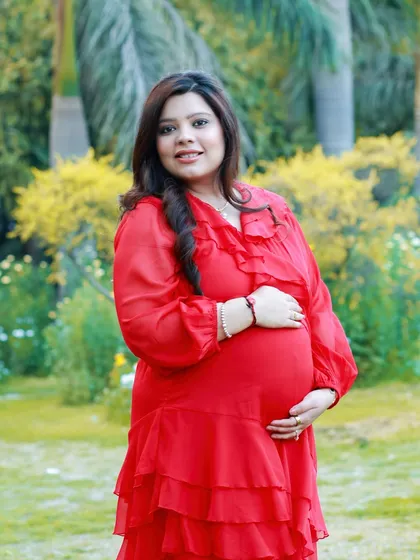 A classic solo maternity portrait that radiates pure joy. The vibrant red dress stands out beautifully against the soft greens of the park, highlighting that special pregnancy glow in natural light.