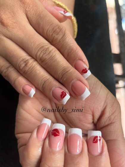 A classic French manicure with a playful twist. This design features a crisp white tip on a square nail shape, with a cute red kiss print accent on a few nails.