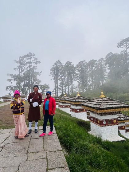 Travelers from our group posing with our local guide at Dochula Pass. The 108 memorial stupas, known as the Druk Wangyal Chortens, are visible in the background, a famous landmark on the way to Punakha.