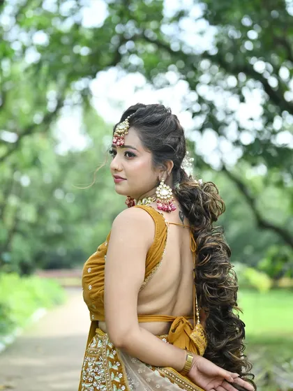 A profile shot of a model in the mustard yellow lehenga, highlighting her elaborate braided hairstyle and the back details of the blouse.