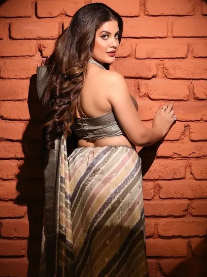 An over-the-shoulder pose that showcases the backless design of the blouse and the flow of the saree. This is a classic pose for ethnic wear catalogues.