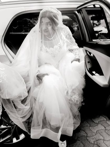 A black and white documentary-style shot of the bride arriving and being helped out of her car.