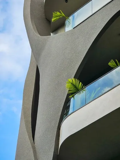 A close-up, raw, and intentional sneak peek of the Lotus Villa's facade. This shot highlights the textured concrete and the deep curves that define its sculptural quality.