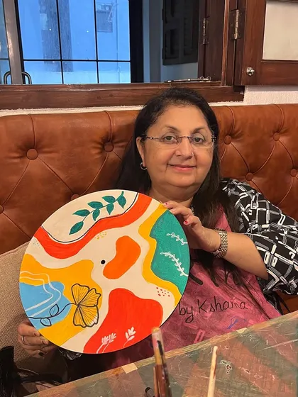 A participant at a kitty party proudly displays the vibrant boho clock she painted. Art parties are a great way to make your get togethers more engaging.