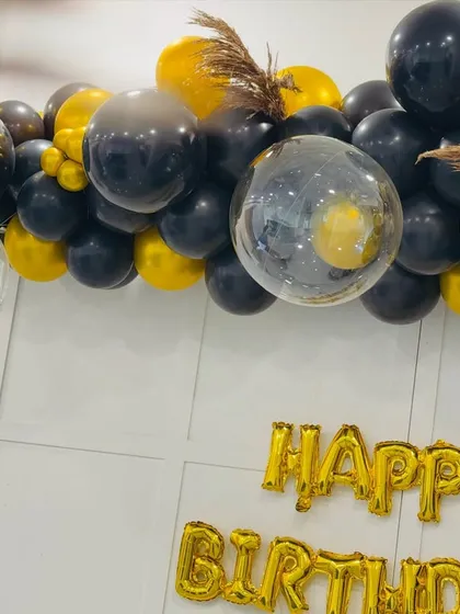 A close-up view of the black and gold balloon decor, showing the mix of textures with clear confetti balloons and dried pampas grass for a modern, chic look.