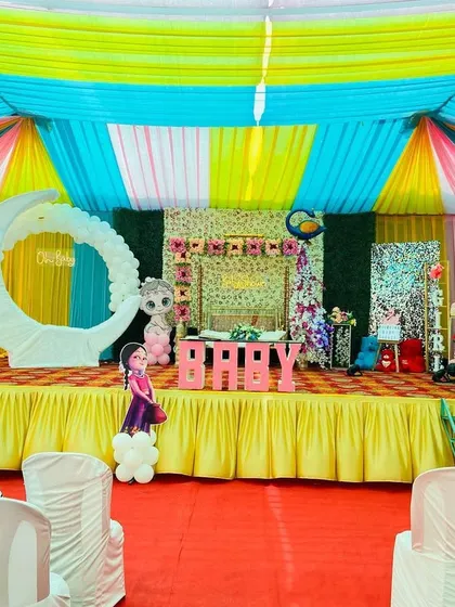 A wide view of the entire baby shower pandal setup, showing the stage, seating arrangement, and colorful ceiling drapes.