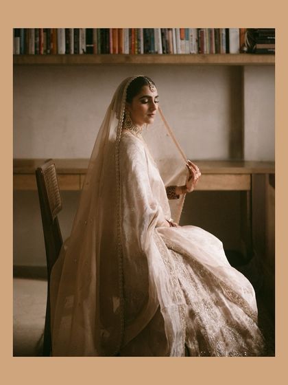 A stunning, artistic portrait of the bride in her elegant, minimalist wedding attire, sitting by a window.