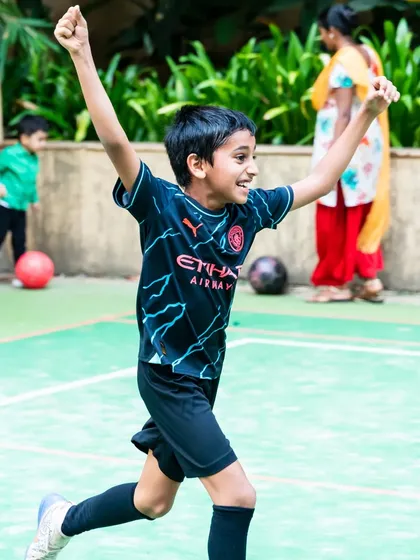 An action shot of the birthday boy celebrating a goal with his arms raised in victory during his football party.