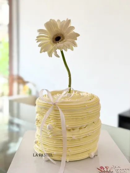 Minimalism at its finest. This single-tier cake features a simple textured buttercream finish and is topped with a single, elegant white gerbera daisy.