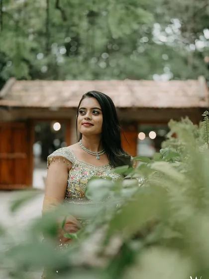 A bride, framed by ferns, looks away with a gentle smile, a soft and romantic portrait.