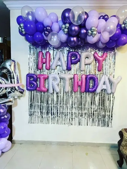 A vibrant 21st birthday decoration at home. The setup features a purple and silver color scheme with a tinsel backdrop and foil balloons for the age.