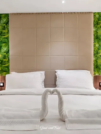 A close-up of the bed in the hotel room, with towels folded into swan shapes. The green accent wall and warm bedside lamps create a tropical and inviting atmosphere.
