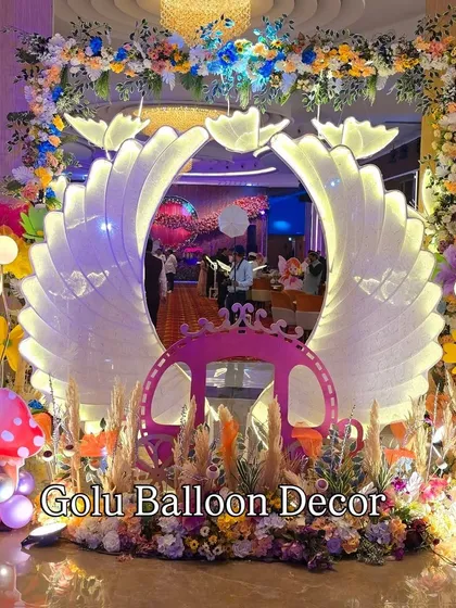 An ethereal fairytale entrance with large, illuminated angel wings, a princess carriage, and magical mushroom props.