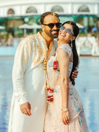 A happy and relaxed portrait of the couple after their Haldi ceremony, embracing by the pool with sunglasses on.