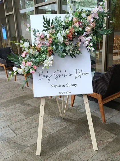A beautiful welcome easel for the "Baby Shah in Bloom" shower, adorned with a lush arrangement of flowers that matches the main decor.