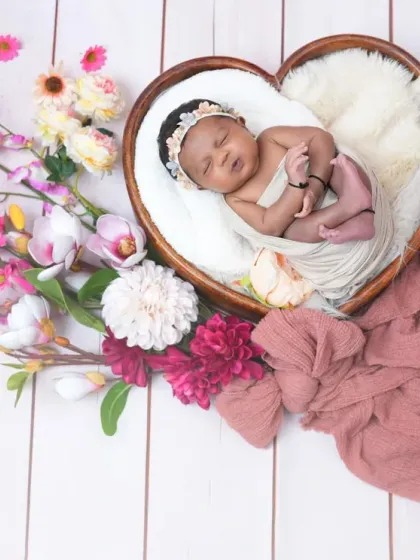 A wide shot showing the full heart-shaped prop and floral arrangement, with the newborn sleeping soundly in the center. The white wood background adds a clean and modern feel.
