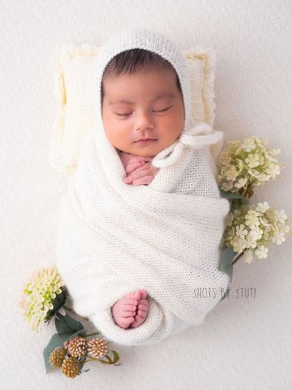 A beautiful newborn in a simple white wrap and bonnet, surrounded by delicate white flowers. This monochromatic setup is pure and angelic.