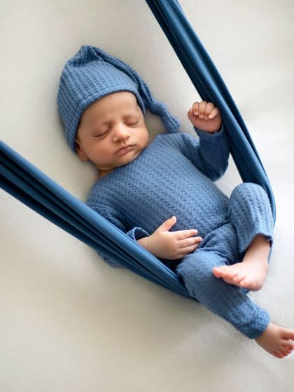 Another angle of the sling pose, showing how the baby is peacefully cradled. The matching blue outfit and hat complete the cohesive look.