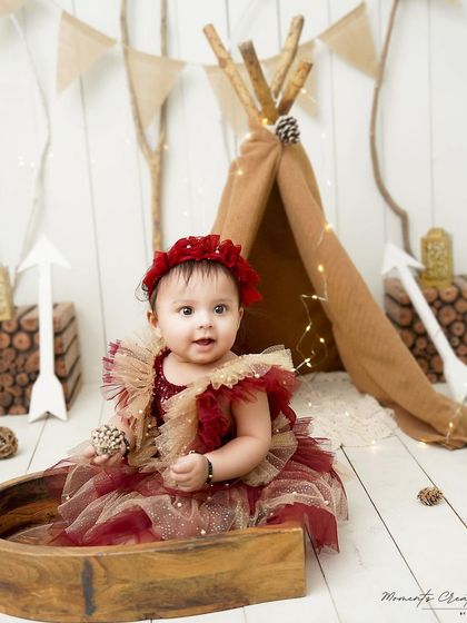 A rustic and charming teepee setup for a one-year-old girl. Her beautiful red and gold dress contrasts wonderfully with the natural, woodsy elements of the set.