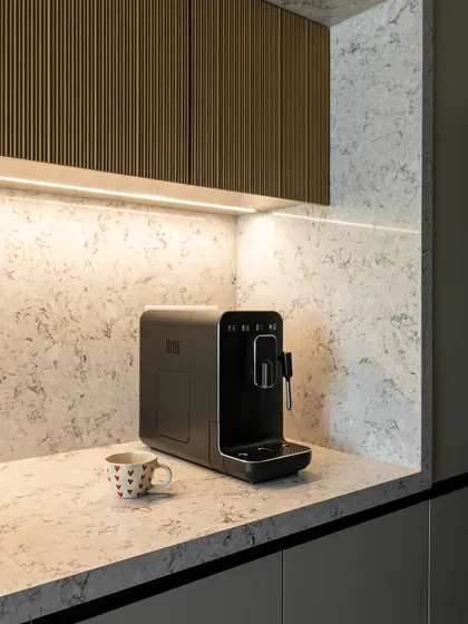 A close-up of fluted wood cabinets above a coffee station. The under-cabinet lighting highlights the texture, adding depth and creating a cozy, inviting corner for your morning brew.