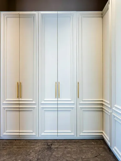 These neo-classical wardrobe doors with their clean white finish and elegant gold handles are a perfect example of timeless design. The intricate molding adds a touch of sophistication to the storage.