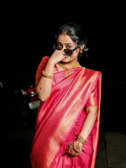 A cheeky and fun pose, with the model playfully adjusting her sunglasses while wearing a traditional pink saree.